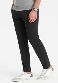 Slim-fit zwarte broek van gestructureerde stof, gecombineerd met witte sneakers met grijze accenten. Het ontwerp is modern en gestroomlijnd.