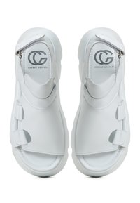 White leather sandals featuring a closed-toe design, wide straps with Velcro closures, and a cushioned sole. Brand logo on the insole.