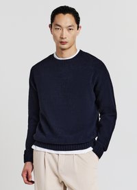 Dunkelblauer Strickpullover mit gerippten Bündchen und Saum, im Crew-Neck-Design, mit strukturiertem Finish. Über einem weißen Hemd und beigen Hosen getragen.