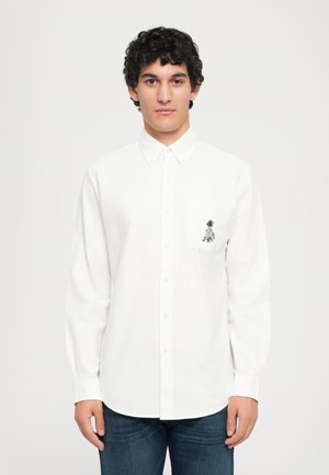 White long-sleeve button-up shirt with a chest pocket featuring a multicolored embroidered design. Cotton fabric, classic collar, straight hem.