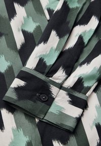 Camicia con colletto caratterizzata da un motivo a zigzag verticale in tonalità di verde, nero e bianco; tessuto testurizzato; singolo bottone nero sul polsino.