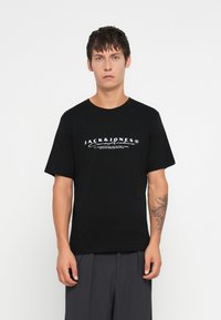 Μαύρο βαμβακερό μπλουζάκι με λευκό λογότυπο "JACK & JONES" στο στήθος. Κλασικός στρογγυλός γιακάς και κοντά μανίκια, με λεία υφή.