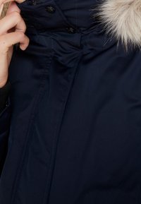Navy blue outerwear jacket with a faux fur collar. Features a zip closure, snap buttons, and ribbed cuffs for added warmth.