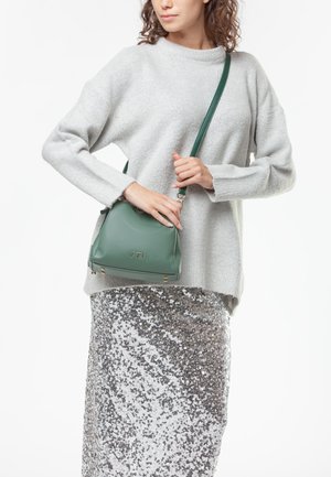 Borsa a tracolla in pelle verde con un design strutturato, dotata di hardware dorato e di una tracolla removibile, abbinata a un maglione grigio e a una gonna di paillettes.