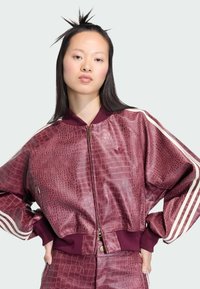 Bordo bomber jakna s uzorkom krokodila, sa zatvaračem, rebrastim manžetama i donjim rubom. Sadrži bijele pruge duž rukava; logo prikazan na prsima.