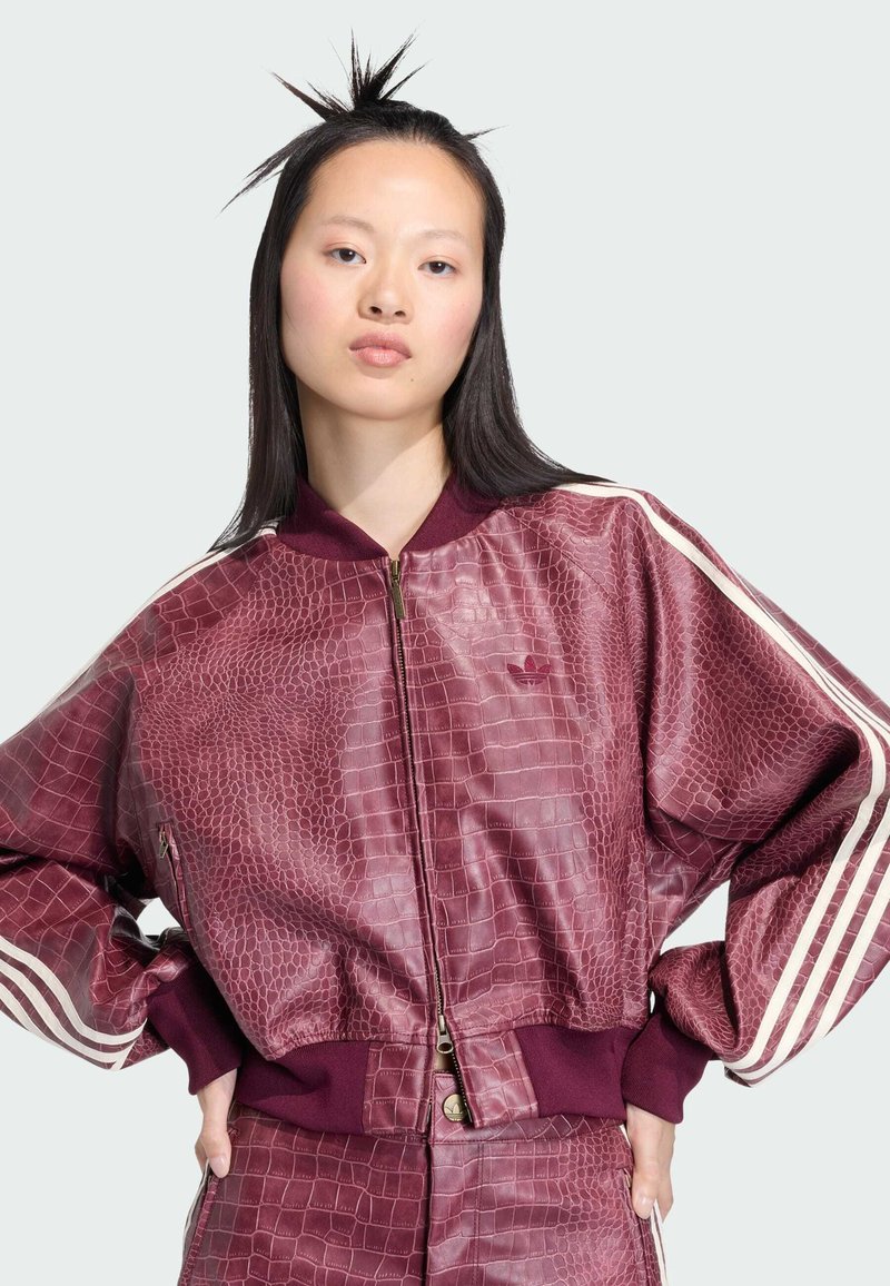 Veste bomber en simili-cuir marron au motif crocodile avec fermeture éclair, poignets et ourlet côtelés. Présente des rayures blanches le long des manches ; logo affiché sur la poitrine.