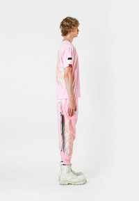 Camisa rosa de manga corta con diseño de alas en la parte posterior, combinada con joggers a juego que presentan acentos brillantes. Botas blancas de gran resistencia completan el conjunto.