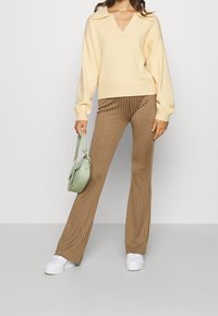 Ljusgul V-ringad tröja, ribbade bruna vida byxor, mintgröna handväska och vita skor. Fokusera på mjuka tyger och texturerade mönster.