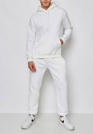Hoodie en mélange de coton blanc avec poche avant, capuche à cordon et jogging ajusté assorti. Coupe décontractée, associé à des sneakers blanches.