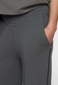 Pantaloni sportivi grigi con una cintura testurizzata, tasche laterali e un accento ricamato "10" sulla parte inferiore della gamba. Tessuto liscio.