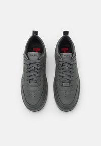 Gray sneakers with a smooth leather texture, featuring a perforated toe area, gray laces, and red accents on the insole and logo.