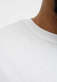 Camiseta de algodón blanca con cuello redondo y textura suave, que presenta un leve patrón jaspeado cerca del cuello.