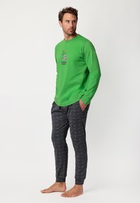 Camisa verde de manga larga con un gráfico juguetón y pantalones oscuros con un diseño estampado que incluye motivos verdes, confeccionados en una tela suave, de corte informal.