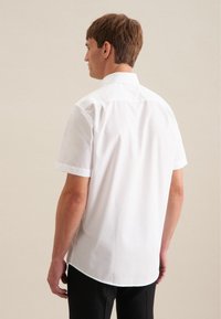 Chemise blanche à manches courtes en coton, dotée d'un col classique, d'un ourlet légèrement arrondi et d'une texture lisse et fraîche.