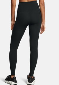 Μαύρα κολάν με ψηλή μέση από ελαστικό ύφασμα, με ομαλή υφή και ελάχιστες ραφές, συνδυασμένα με μαύρα αθλητικά παπούτσια.