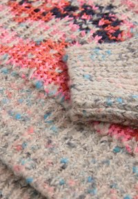 Tissu tricoté multicolore présentant un mélange de textures douces. Les couleurs dominantes incluent un gris muted, du rose et du bleu avec un détail de motif varié.