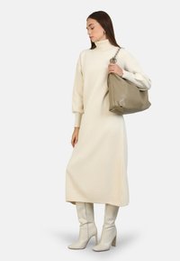 Vestido de punto color crema con cuello alto y mangas abullonadas, combinado con un bolso beige suave y botas blancas de tacón hasta la rodilla.