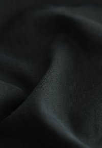 Texturiertes schwarzes Gewebe mit einer weichen Webart, das in Falten hängt und subtile Schatten und Highlights über die Oberfläche erzeugt.
