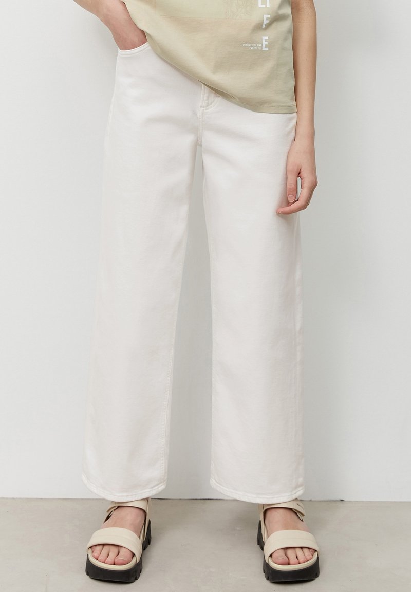 Vita vida jeans i bomullstyg med hög midja. Kombinerat med beige plattformssandaler med ett band över tårna.