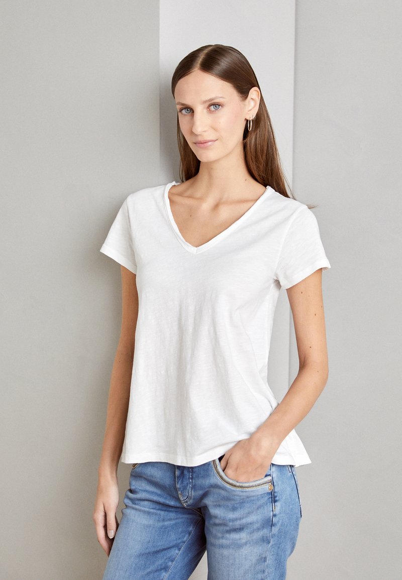 Weißes Baumwoll-T-Shirt mit V-Ausschnitt und kurzen Ärmeln, mit lockerem Schnitt und weicher Textur, kombiniert mit hellblauen Jeans.