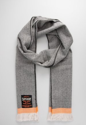 Szary szalik z wzorem jodełki, z pomarańczowym pasem i białymi frędzlami na końcach, z czarną i pomarańczową metką marki Superdry.