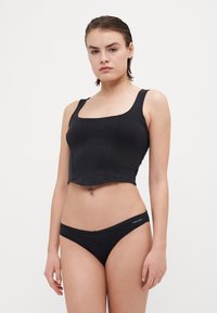 Must mängub must lühike tank top laia rihmaga ja ruudukujulise kaelusega, mis on ning koos mustade bikiinialustega, millel on minimalistlik logo vöökohtadel.