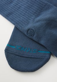 Navy blue socks with ribbed texture, featuring a circular logo and a teal accent stripe with the word "STOCK." Smooth, knit fabric.