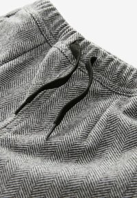 Gråt herringbone-mønstret stof med en tekstureret overflade, prydet med en snoretræk i taljen med sorte detaljer.