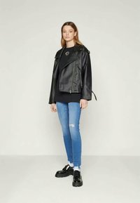 Chaqueta de biker de cuero negro con cremallera asimétrica, llevada sobre una blusa negra, combinada con jeans rotos de color azul claro y zapatos chunky negros.