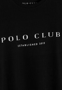 Černé bavlněné tričko s bílým textem "POLO CLUB" a nápisem "ESTABLISHED 2012" pod ním, kulatý výstřih, hladká textura, volný střih.