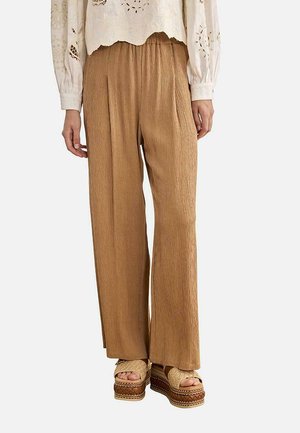 Pantalones de pierna ancha beige con tela texturizada, combinados con sandalias de plataforma abiertas y una blusa blanca de manga larga con bordados.
