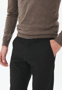 Suéter marrón tejido con puños acanalados, combinado con pantalones negros de textura suave y diseño de frente plano.