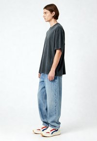 Per didelės pilkos medvilnės marškiniai, šviesiai mėlyni laisvi džinsai ir balti sportiniai bateliai su raudonais ir mėlynais akcentais. Paprastas, kasdieniškas drabužių derinys.