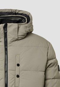 Olive žalia pamušalinė striukė su aukšta apykakle, juodu užtrauktuku, priekyje su spaudėmis ir tekstūruotu paviršiumi.