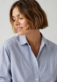 Camicia a maniche lunghe a righe in azzurro chiaro e bianco con colletto a punta e dettaglio dell'inserto angolato. Presenta una vestibilità rilassata e una consistenza liscia.