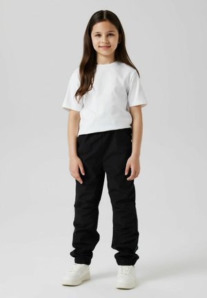 T-shirt en coton blanc à manches courtes, associée à un pantalon noir à poignets élastiques et des baskets blanches. Design simple, palette de couleurs neutres.