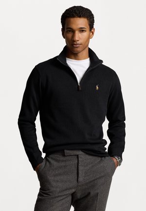 Zwarte zip-up trui met een witte binnenkraag, gecombineerd met grijsgemarmerde broek. Heeft een klein gouden embleem op de linkerborst.