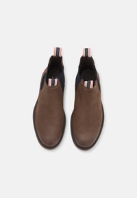 Botas de cuero marrón hasta el tobillo con un panel de malla azul marino, que cuenta con una lengüeta a rayas. Punta redondeada y suela plana. Textura suave en general.