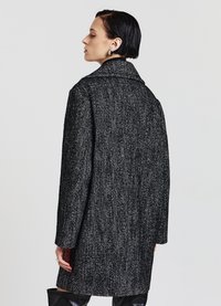 Cappotto a motivo pied de poule in bianco e nero, con ampio colletto e maniche lunghe, realizzato in un tessuto testurizzato.