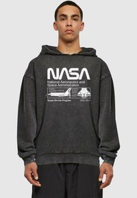 Sweatshirt en coton gris avec capuche, comportant un grand logo NASA blanc et des détails de mission imprimés sur le devant. Design ample.