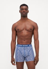Boxers en coton bleu avec un motif, de forme ajustée et une ceinture élastique arborant le logo "BJÖRN BORG". Le matériau semble lisse et extensible.