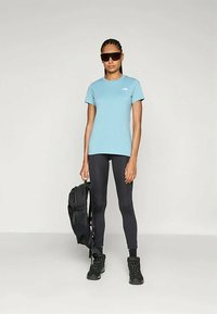 Svetlo modra kratka majica s kratkimi rokavi in logotipom, črne legice, črn nahrbtnik in čevlji. Gladka tkanina, prilega se telesu, primerna za aktivno obleko.