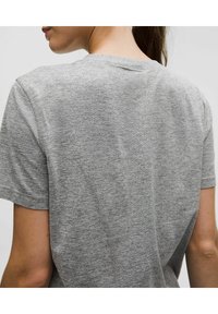 Grå t-shirt med kort ärm och texturerat mönster, rund halsringning och avslappnad passform. Sömdetalj löper vertikalt längs ryggen.