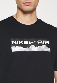 Black cotton T-shirt featuring a rectangular white and gray graphic with "NIKE AIR" text and cloud imagery across the chest.