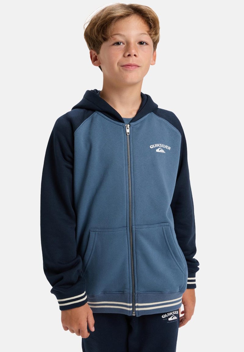 Hooded zip-up sweatshirt gemaakt van zachte stof, met een blauwe body en marineblauwe mouwen, witte accenten en zakken aan de voorkant. Quiksilver-logo weergegeven.