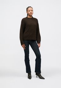 Bruine gebreide trui met een ronde hals, lange mouwen, gecombineerd met donkerblauwe wijde jeans en zwarte puntige enkellaarsjes.