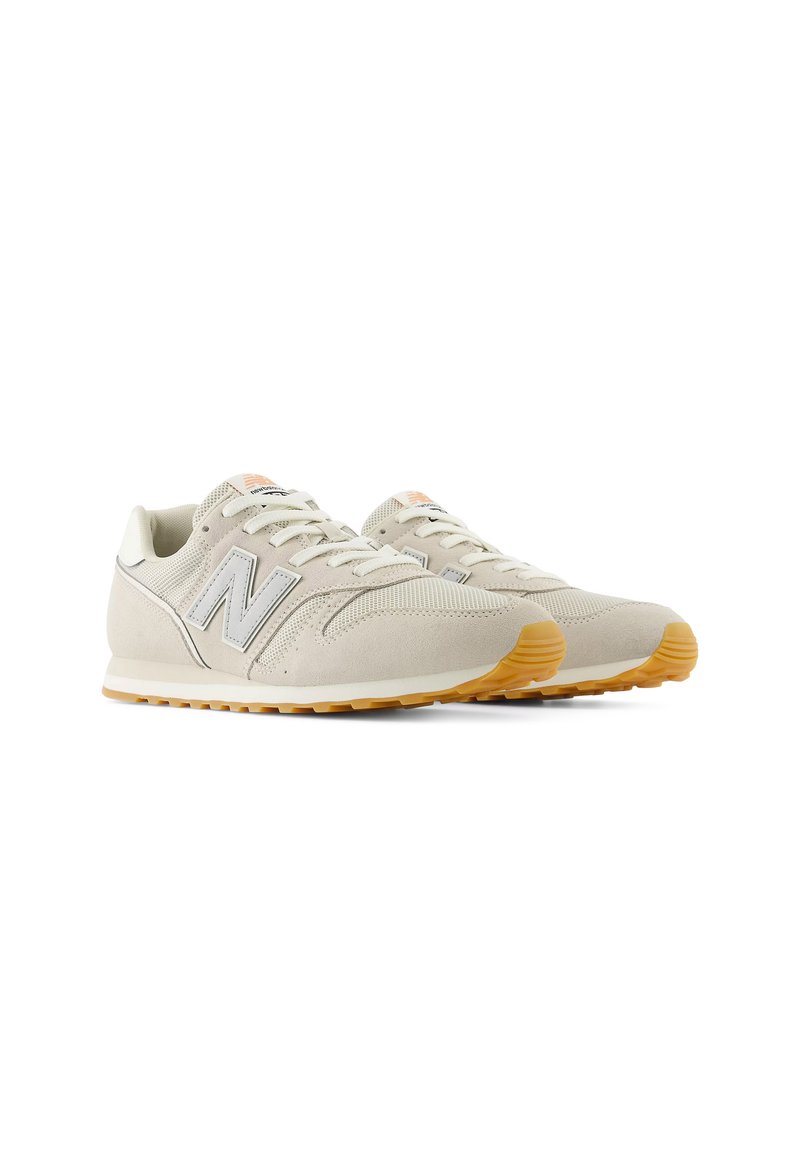 Zapatillas beige claro con materiales de ante y malla, que presentan un logotipo plateado prominente, acentos naranjas y una suela de goma con un patrón texturizado.