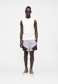 Haut blanc sans manches, short à motifs avec des accents bordeaux, et baskets grises. Tenue décontractée, texture lisse, motifs géométriques.