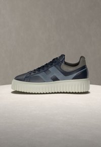 Basket basse bleu marine avec semelle blanche épaisse rainurée et col de talon en daim gris sur fond neutre.