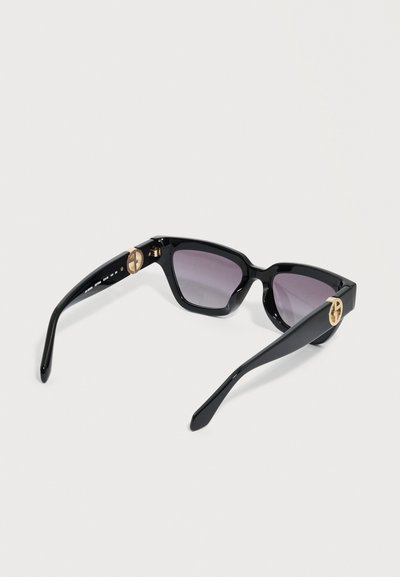 Μαύρα ορθογώνια γυαλιά ηλίου με σκουρόχρωμους φακούς με διαβάθμιση και χρυσά κυκλικά λογότυπα στα μπράτσα, πάνω σε λευκό φόντο.